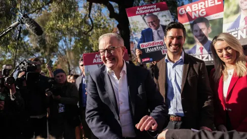 رئيس الوزراء الأسترالي أنتوني ألبانيز مبتسم وسط مؤيديه، مع لافتات دعائية لحزبه، مما يعكس أجواء الحملة الانتخابية.