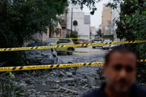 تظهر الصورة شارعاً مدمراً في البحرين، محاطاً بشريط الشرطة الأصفر، مع وجود سيارة متضررة وحطام في الخلفية، مما يعكس آثار الضربات الإيرانية.