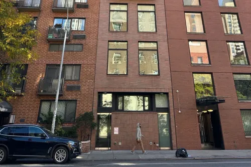 مبنى سكني متواضع في مانهاتن، حيث يُزعم أن ألعاب بوكر غير قانونية كانت تُجرى داخله، يظهر فيه شخص يمشي بجانب سيارة.