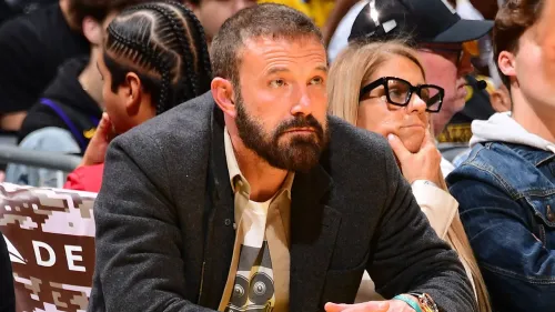 بن أفليك يجلس في مدرجات مباراة، مع التركيز على تعابير وجهه الجادة، بينما يظهر خلفه مشجعون آخرون.