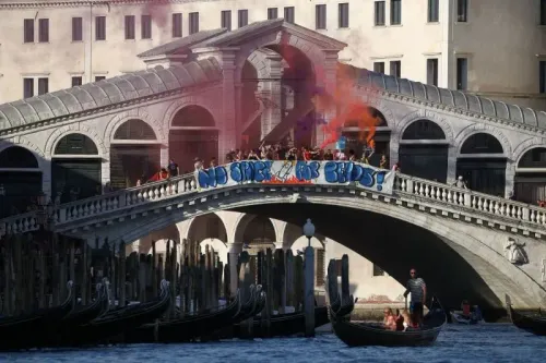 محتجون يتظاهرون على جسر في البندقية ضد جيف بيزوس، حاملين لافتة "لا مكان لبيزوس"، مع دخان ملون يحيط بهم.