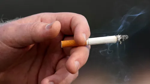 يد تحمل سيجارة مشتعلة، تشير إلى اقتراح إدارة الغذاء والدواء الأمريكية للحد من مستويات النيكوتين في السجائر لتقليل الإدمان.