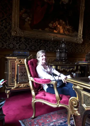 كاثي رويملر تجلس في كرسي فاخر داخل غرفة مزينة بأثاث أنيق، تعكس العلاقة المهنية المعقدة بينها وبين جيفري إبشتاين.