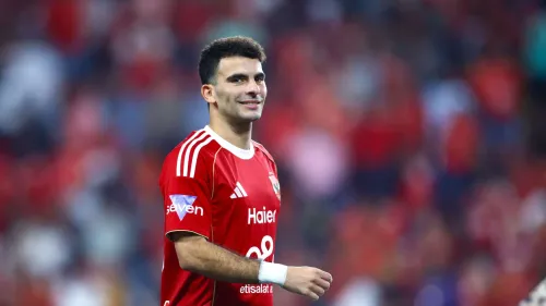 لاعب كرة قدم يرتدي زي الأهلي الأحمر وسط جمهور غفير في استاد، يعكس أجواء المنافسة في الدوري السعودي والمشاريع الطموحة للنادي.