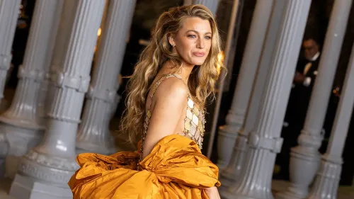 بلake ليفلي ترتدي فستانًا برتقاليًا أنيقًا في حدث رسمي، مع خلفية من أعمدة بيضاء، تعكس أجواء احتفالية.