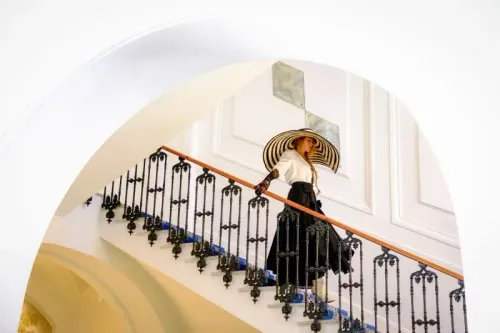 امرأة ترتدي فستانًا أسود وقبعة عريضة أثناء نزولها على الدرج، مع تفاصيل معمارية أنيقة في الخلفية، تعكس أجواء فيلم "خدمة بسيطة أخرى".