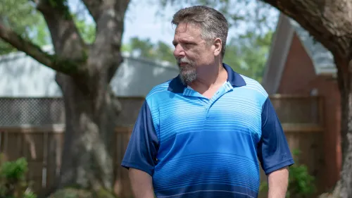 رجل في منتصف العمر يرتدي قميصًا أزرق مخططًا يقف في حديقة، يبدو عليه التأمل، في سياق دعوى قضائية ضد شركة بوينج.