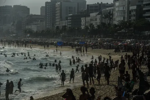 شاطئ إيبانيما في ريو دي جانيرو مزدحم بالزوار، حيث يسبح البعض في المياه بينما يستمتع الآخرون على الرمال، وسط مبانٍ شاهقة.