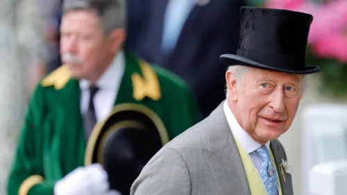 الملك تشارلز الثالث يرتدي بدلة رسمية وقبعة عالية، مع وجود شخص آخر خلفه، في مناسبة رسمية تعكس التقاليد الملكية.