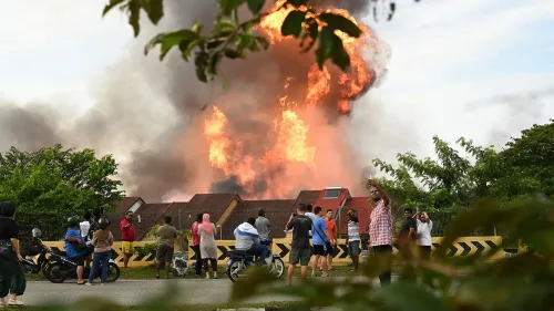 حريق هائل يندلع في ضاحية ماليزية، مع تصاعد اللهب والدخان، بينما يتجمع المواطنون لمشاهدة الحادث.