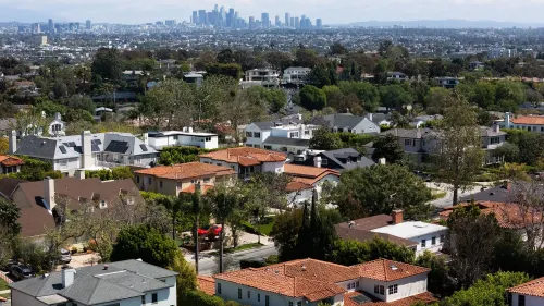 منظر جوي لحي سكني في الولايات المتحدة، يظهر منازل مختلفة مع خلفية لمدينة، يعكس ارتفاع تكاليف ملكية المنازل بعد جائحة كوفيد-19.