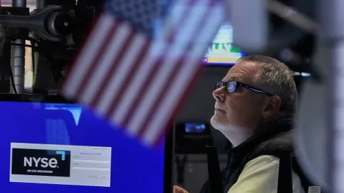 تاجر في بورصة نيويورك يراقب الشاشة، مع وجود علم أمريكي في الخلفية، في ظل تباين آراء المستثمرين حول السوق.