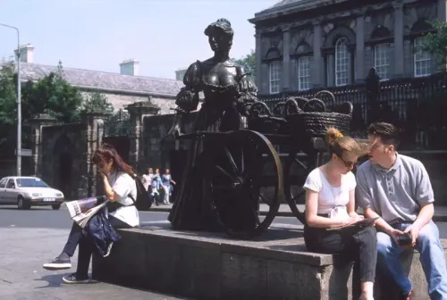 تمثال مولي مالون البرونزي في دبلن، يظهر امرأة تحمل عربة، بينما يجلس سائحان بالقرب منها. تبرز القصة وراء التمثال من خلال تفاعل الزوار معه.