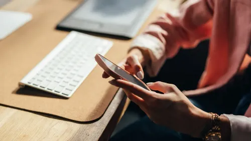 شخص يستخدم هاتفه المحمول أثناء العمل على مكتب، مع وجود لوحة مفاتيح في الخلفية، مما يعكس تأثير وسائل التواصل الاجتماعي على بيئة العمل.