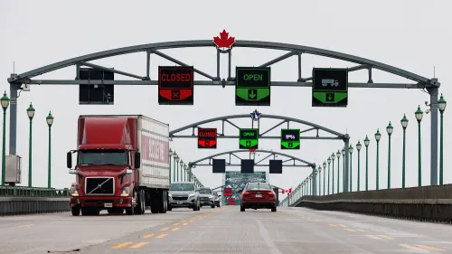 جسر يربط كندا بالولايات المتحدة، يظهر لافتات تشير إلى حالة المرور، مع شاحنة وسيارات تسير في الاتجاهين، في سياق التوترات التجارية.