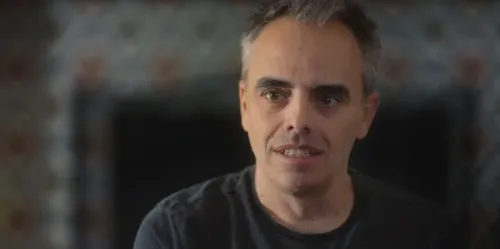 شخص يتحدث بجدية حول حادثة إطلاق النار القاتل في موقع تصوير فيلم "Rust"، مع خلفية غير واضحة تعكس مشاعر الحزن والصدمة.