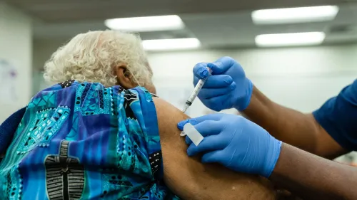 تظهر الصورة شخصًا مسنًا يتلقى لقاح كوفيد-19 في عيادة طبية، مما يعكس أهمية التطعيم للفئات الأكثر عرضة للخطر.