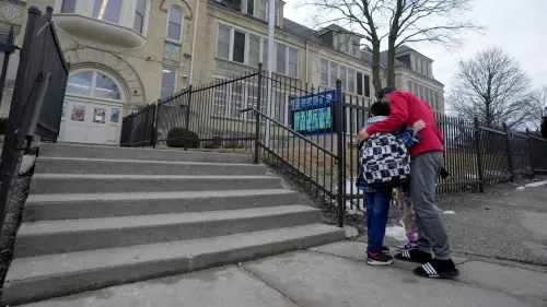 طفل يحمل حقيبة مدرسية يحتضنه شخص بالغ أمام مدخل مدرسة في ميلووكي، في سياق قلق بشأن مستويات الرصاص في المدارس.