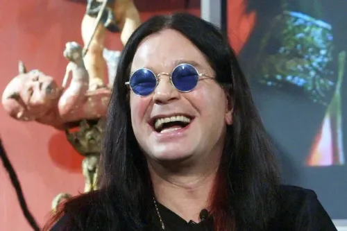 أوزي أوزبورن مبتسم في صورة قديمة، مع نظارات شمسية، تعبيراً عن شخصيته الفريدة وتأثيره في عالم موسيقى الهيفي ميتال.