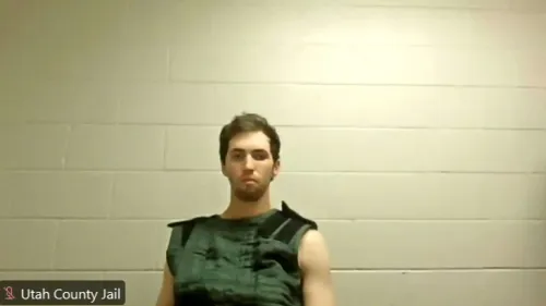 شاب يبلغ من العمر 22 عامًا، متهم بقتل ناشط سياسي، يظهر في جلسة محكمة مرتديًا سترة الحراسة، مع خلفية جدران رمادية.