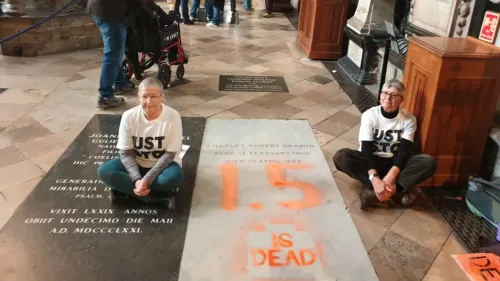 نشطاء بيئيون يجلسون قرب قبر تشارلز داروين في دير وستمنستر، مع عبارة \"1.5 مات\" مرسومة باللون البرتقالي، في احتجاج ضد أزمة المناخ.