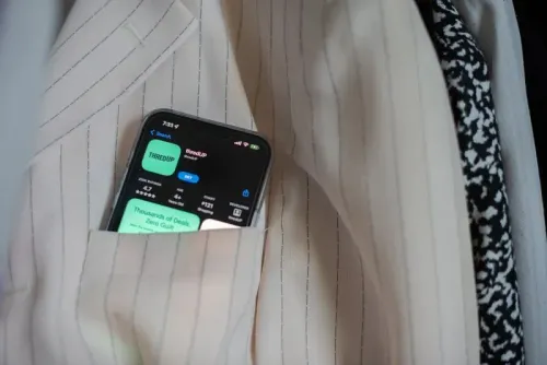 تظهر الصورة هاتفًا محمولًا داخل جيب بدلة، يعرض تطبيق ThredUp، الذي يروج للموضة المستدامة والملابس المستعملة.