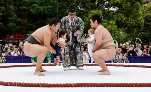 مصارعو سومو يحملون أطفالًا في حلبة السومو خلال احتفال ياباني تقليدي، وسط جمهور كبير، للاحتفال بيوم الطفل.
