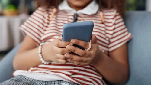 طفل صغير يجلس على أريكة، ممسكًا بهاتف ذكي، مما يعكس تأثير التكنولوجيا على الأطفال وزيادة مخاطر الاعتداء الجنسي عبر الإنترنت.