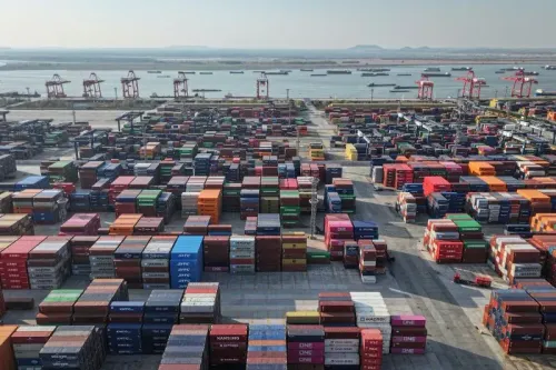 صورة لميناء حاويات مزدحم يحتوي على العديد من الحاويات الملونة، مع رافعات في الخلفية، تعكس تأثير الحرب التجارية بين الولايات المتحدة والصين.
