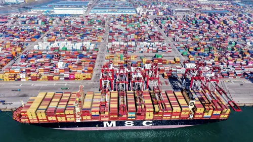 سفينة شحن كبيرة محملة بالحاويات في ميناء مزدحم، تعكس نشاط التجارة الدولية وتأثير التعريفات الجمركية على الاقتصاد الصيني.