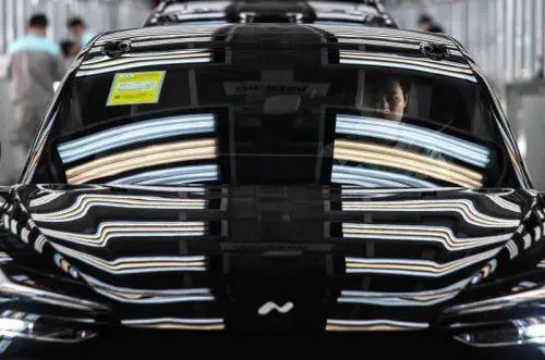 شخص يجلس داخل سيارة كهربائية سوداء في مصنع، مع انعكاسات الأضواء الساطعة على الزجاج، مما يعكس تقدم الصين في صناعة السيارات الكهربائية.