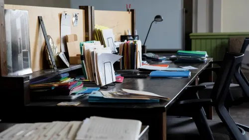 مكتب فوضوي يحتوي على ملفات ملونة وأوراق متناثرة، مما يعكس حالة من الارتباك الإداري في سياق مناقشة أصول كوفيد-19.