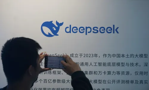 شخص يُصوّر شعار شركة DeepSeek على حائط يحتوي على معلومات حول نموذجها الجديد للذكاء الاصطناعي، مما يعكس الابتكار في هذا المجال.