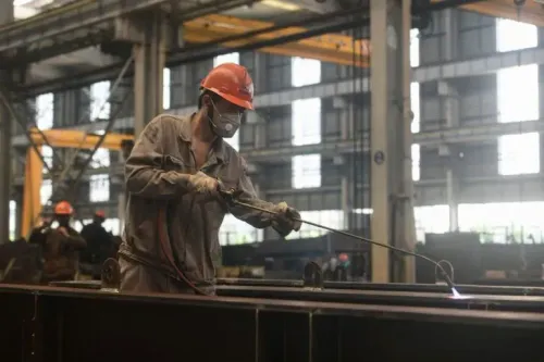 عامل يرتدي خوذة وقناعًا يعمل على لحام المعادن في مصنع، مما يعكس نشاط القطاع الصناعي في الصين وسط تحديات التجارة العالمية.