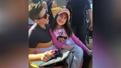 طفلة مبتسمة ترتدي قبعة وردية وتجلس بجوار صبي، في أجواء عائلية. تعكس الصورة لحظات من البراءة والسعادة.