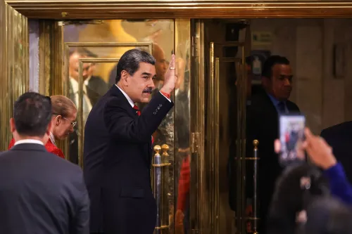 نيكولاس مادورو، رئيس فنزويلا، يلوح بيده أثناء مغادرته من مدخل فخم، محاطًا بمساعدين، في سياق التوترات السياسية مع الولايات المتحدة.