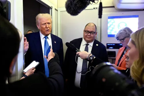 ترامب يتحدث مع الصحفيين في ممر الطائرة، بينما يحيط به عدد من المراسلين، مع وجود شاشات عرض خلفهم.