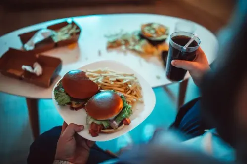 وجبة سريعة تتكون من برجرين مع بطاطا مقلية وكوب من المشروب الغازي، مع بقايا طعام على الطاولة، تعكس تأثير الأطعمة فائقة المعالجة.