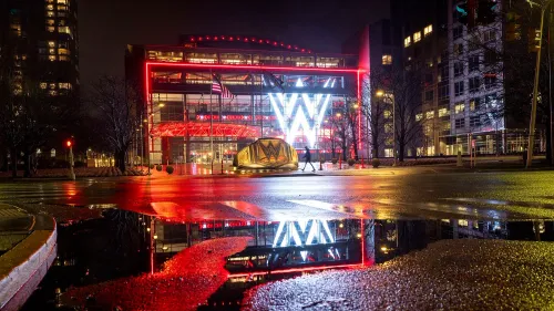 مبنى WWE مضاء بألوان زاهية في الليل، مع انعكاسات على الرصيف، يعكس الأجواء المحيطة بقضايا الاعتداء الجنسي والاتجار بالبشر.