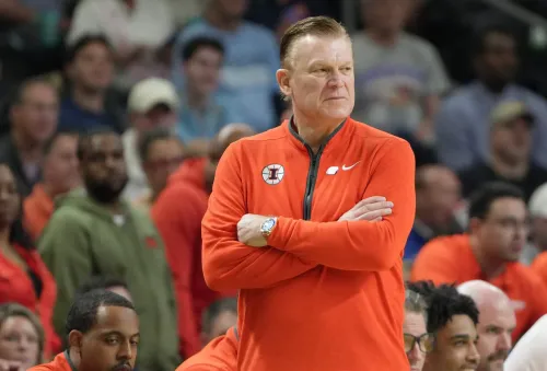 مدرب كرة السلة براد أندروود يقف مع ذراعيه متقاطعتين، يعكس شخصية قوية ومهيمنة، وسط جمهور في ملعب رياضي.