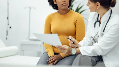 امرأة ترتدي سترة صفراء تجلس أمام طبيبة تتحدث معها في عيادة طبية، مع التركيز على أهمية علاج التهاب المهبل البكتيري.