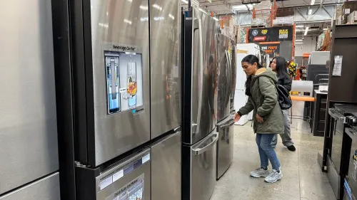 امرأة تتفقد ثلاجة في متجر للأجهزة المنزلية، مع وجود ثلاجات أخرى في الخلفية، تعكس زيادة إنفاق المستهلكين.