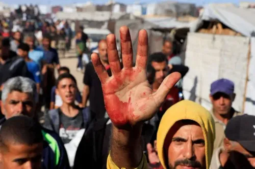 رجل فلسطيني يرفع يده الملطخة بالدماء وسط حشد من الأشخاص في غزة، معبرًا عن معاناتهم خلال توزيع المساعدات الإنسانية.