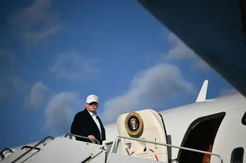 دونالد ترامب يصعد إلى طائرة رئاسية، مع شعار "اجعل أمريكا عظيمة مرة أخرى" على قبعة. الصورة تعكس التحديات الأمنية المتعلقة بالطائرة القطرية المقترحة.