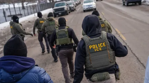عناصر من قوات إنفاذ قوانين الهجرة والجمارك (ICE) يسيرون في شارع، مما يعكس التوترات بين الولايات الحمراء والزرقاء حول سياسات الهجرة.