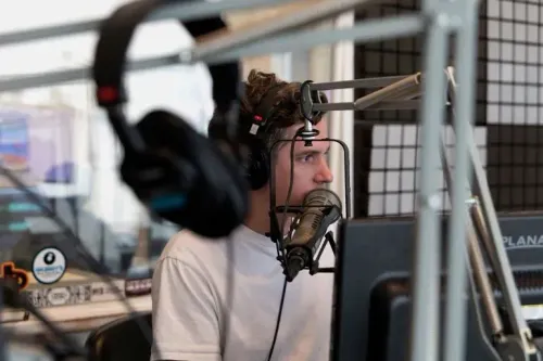 شخص يجلس أمام ميكروفون في استوديو إذاعي، مع سماعات على أذنه، يعكس تأثير خفض التمويل على الإعلام العام.