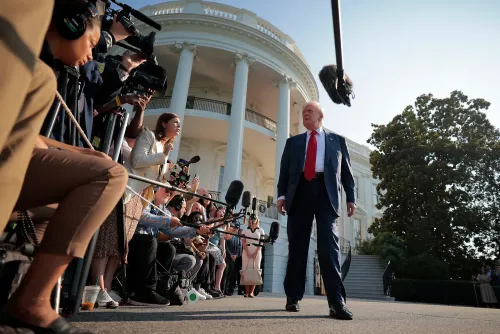 رجل يرتدي بدلة رسمية يقف أمام البيت الأبيض محاطًا بالصحفيين والكاميرات، يعكس أجواء التوتر السياسي حول تمويل الإعلام العام.