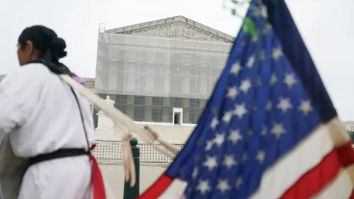 محتجون يقفون أمام المحكمة العليا الأمريكية، مع وجود علم أمريكي في المقدمة، بينما تُغطى واجهة المبنى بشبكة.