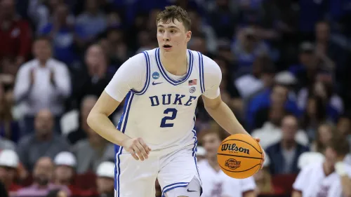 كوبر فلاج، لاعب كرة سلة من جامعة ديوك، يحمل الكرة أثناء مباراة، مستعد للتسجيل، مع جمهور خلفه.