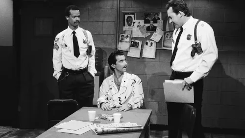 مشهد من برنامج "ساترداي نايت لايف" يظهر ثلاثة رجال في غرفة، مع رسومات وصور على الجدران، مما يبرز لحظة درامية من الكوميديا.